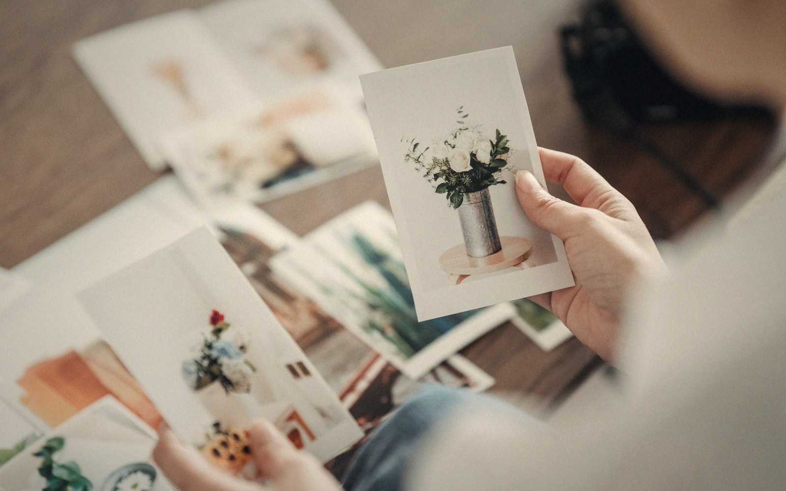 Hands holding a printed photo of flowers in a vase over scattered prints